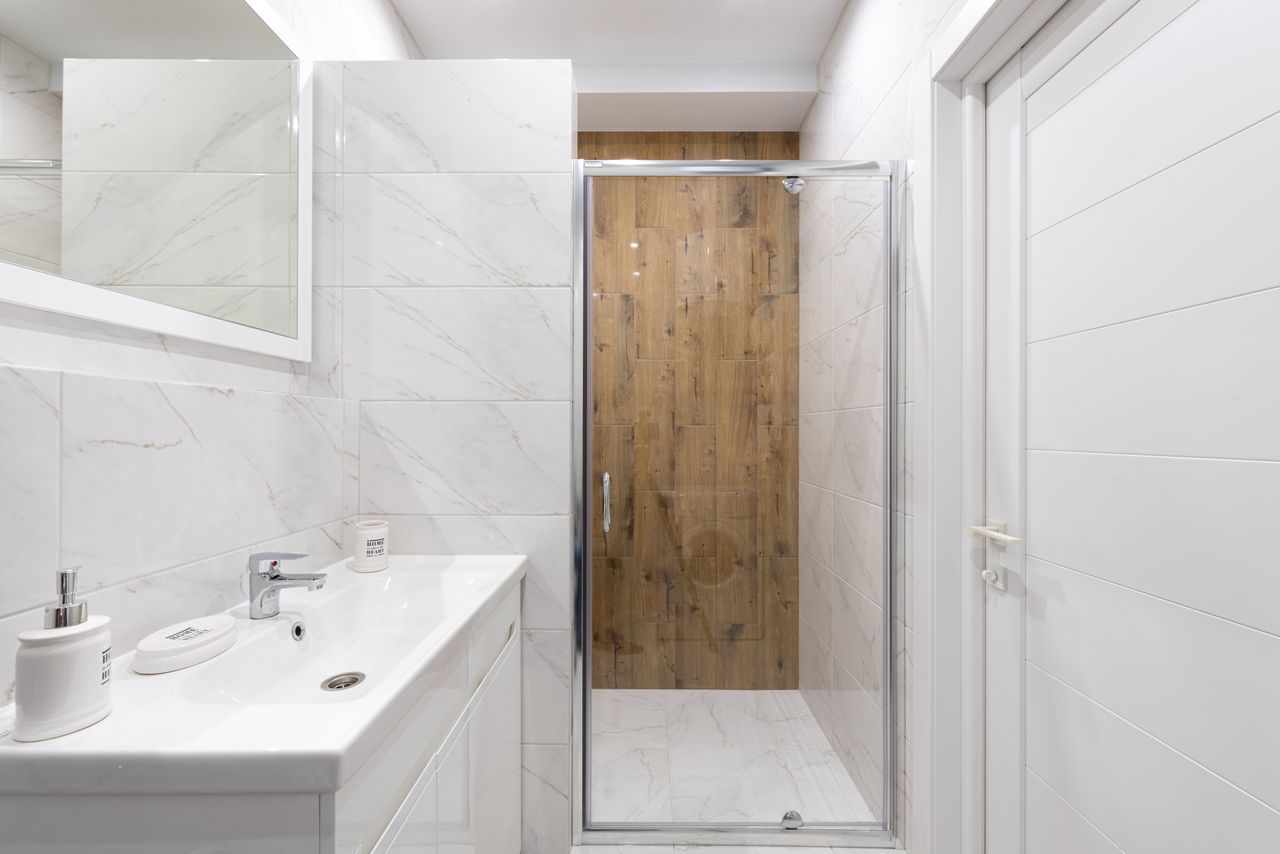 Modern bathroom with washstand under rectangular mirror on tiled wall against shower room in light house