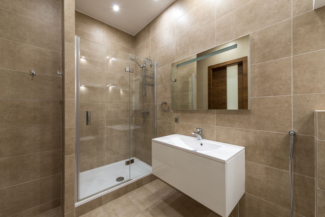 Elegantly designed modern bathroom featuring a glass shower, wall mirror, and large ceramic tiles.